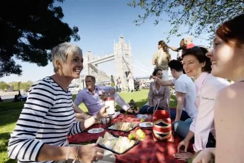 Gruppe von Reisenden genießen ein Picknick im Park mit Blick auf die Tower Bridge in London.