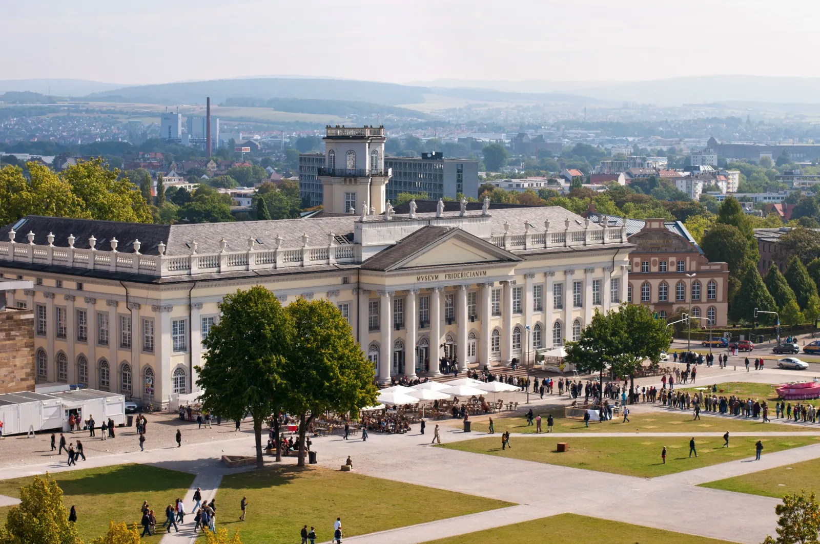 Man sieht die Ausstellungshalle der documenta von oben und viele Menschen auf dem Vorplatz.
