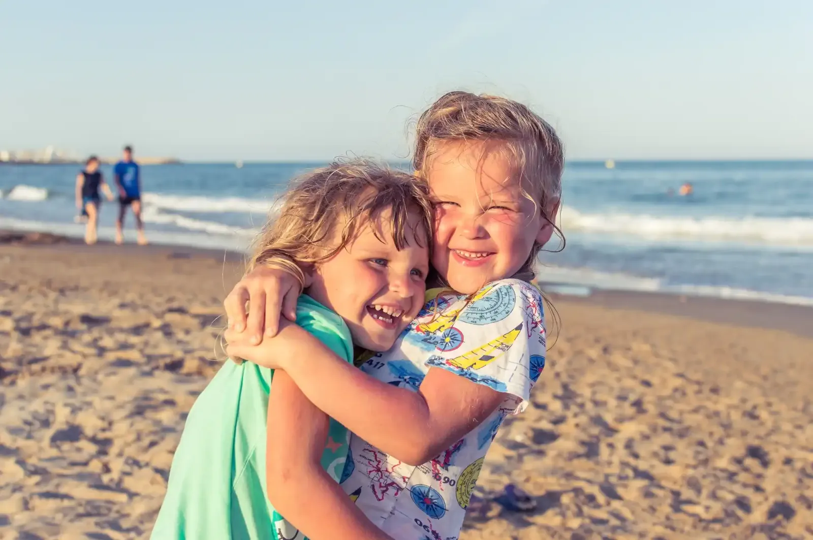 Zwei fröhliche Kinder umarmen sich am Strand.