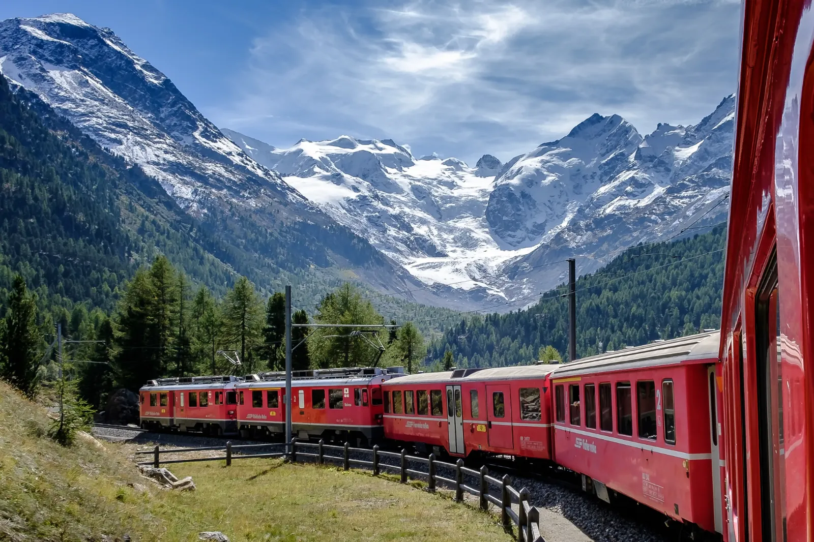 Eine Eisenbahn fährt durch eine Landschaft mit schneebedeckten Bergen im Hintergrund.