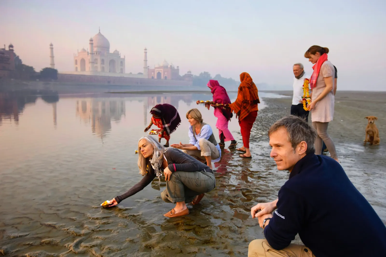 Eine Gruppe von Menschen an einem Fluss, mit dem Taj Mahal im Hintergrund.