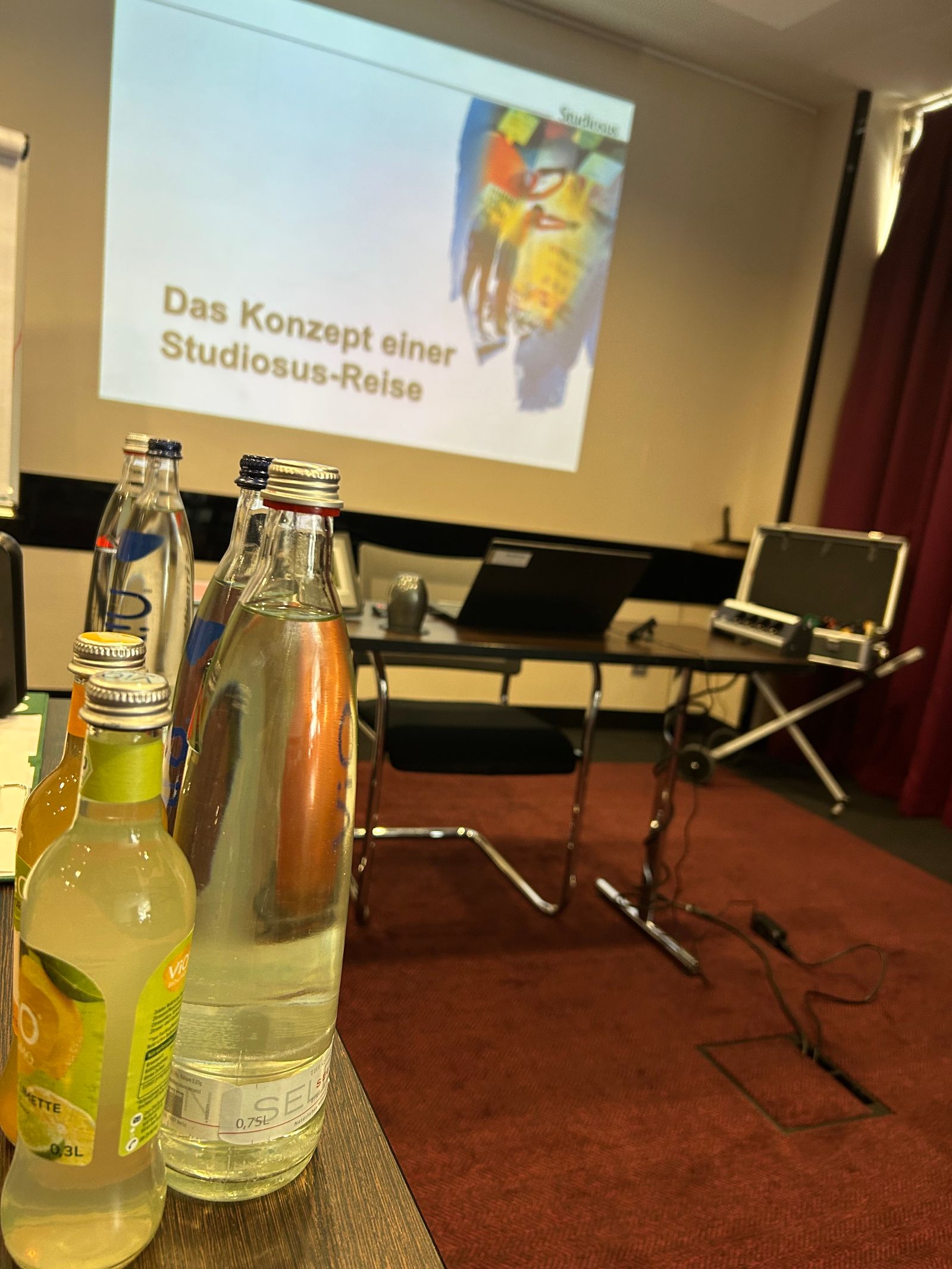 Live Bild eines unserer Seminare "Reiseleitung bei Studiosus": Getränke vor der Beamer Projektion auf der steht: "Das Konzept einer Studiosus-Reise"