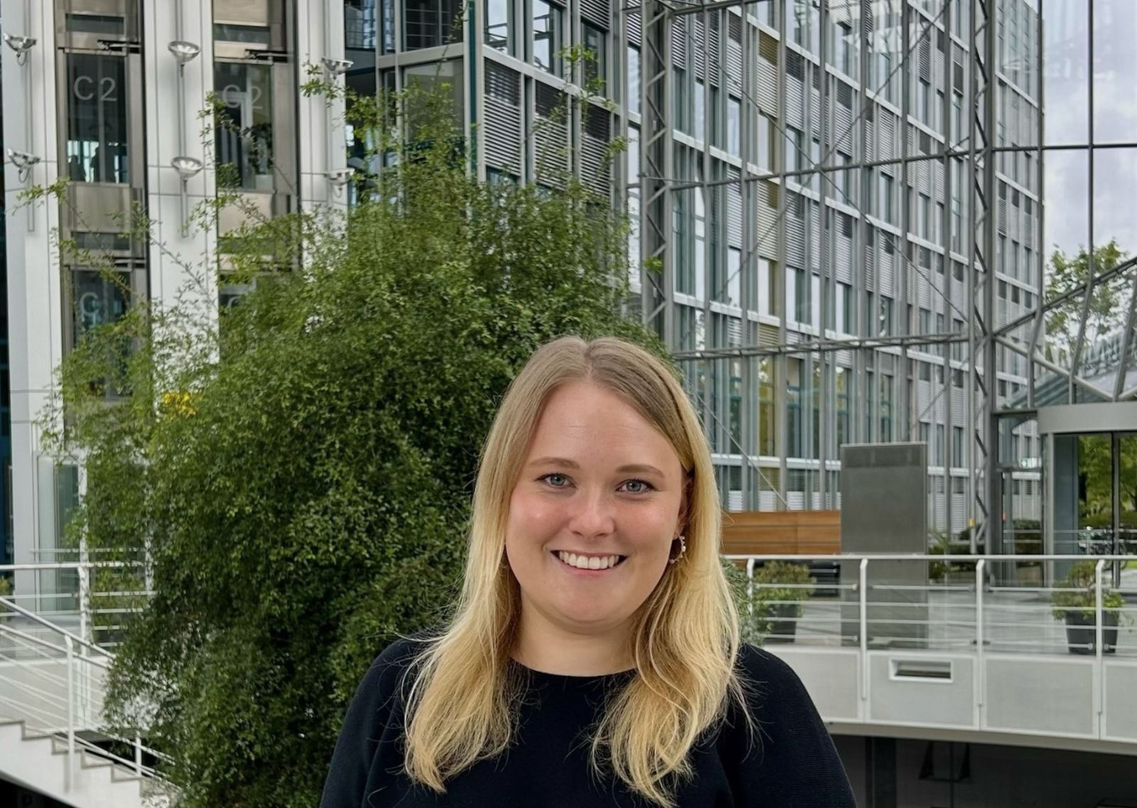 Eine Frau mit blonden Haaren steht in einem Glasgebäude.