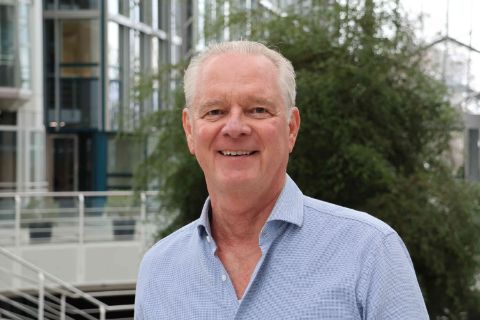 Peter Strub, ehemaliger COO bei Studiosus Reisen München, steht im Münchner Firmensitz und lächelt in die Kamera.