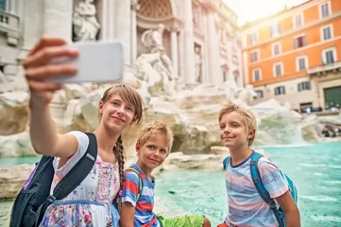 Ein Mädchen steht zusammen mit zwei Jungs vor dem Trevi-Brunnen in Rom und macht von den Dreien ein Selfie.
