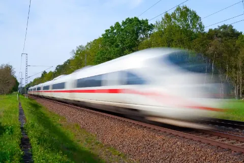 Ein Moderner ICE Zug fährt schnell durch die Landschaft und hinterlässt eine verschwommene Bewegung.
