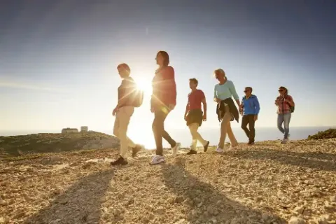 Eine Gruppe von sechs Personen wandert auf einem Bergweg bei Sonnenuntergang.