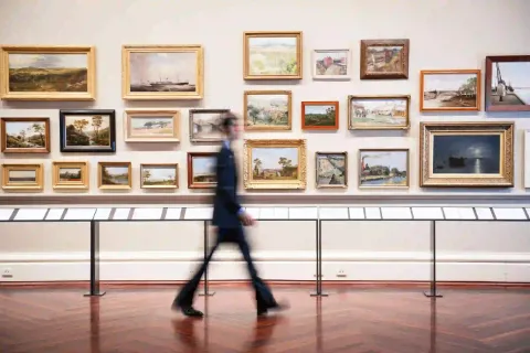 Ein Besucher geht durch eine Kunstgalerie mit verschiedenen Gemälden.