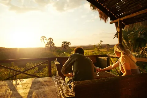 Mann und Frau sitzen auf einer Terrasse mit Blick auf die Natur und den Sonnenuntergang.