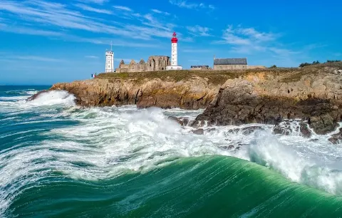 Küstenlandschaft der Bretagne mit Leuchtturm, brechenden Wellen und klarem Himmel.