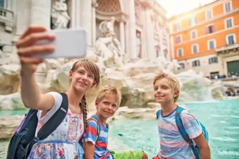 Drei Kinder auf einer Reise nach Rom machen einen Selfie am berühmten Trevi-Brunnen.