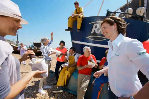 Eine Reisegruppe genießt ein Essen am Strand mit einem Fischerboot im Hintergrund.