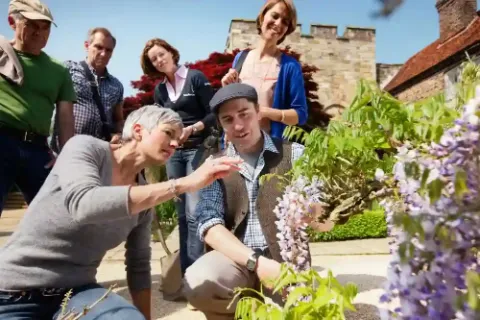 Eine Gruppe von Menschen, die Pflanzen im Garten betrachten und diskutieren.