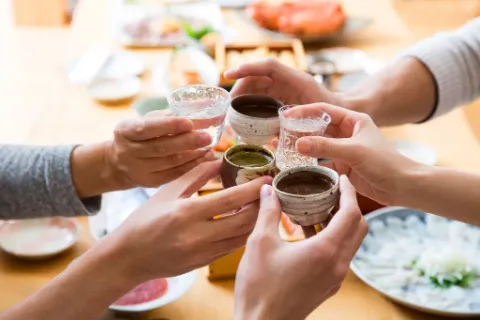 Kleine Gläser und Tassen mit Sake werden bei einer japanischen Mahlzeit angestoßen.