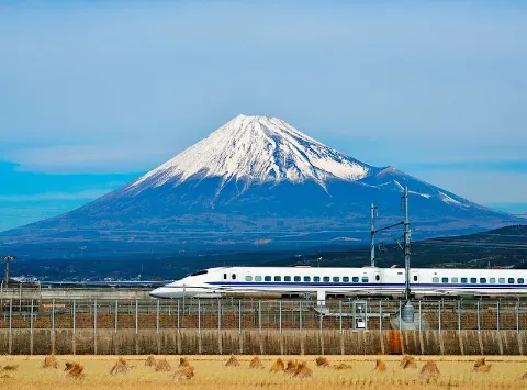 Ein japanischer Hochgeschwindigkeitszug fährt durch eine flache Landschaft am Fuji-Berg vorbei.