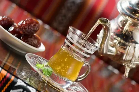 Ein Glas Tee und eine Schale mit Datteln auf einem Tisch mit orientalischem Muster.