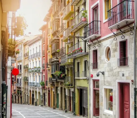 Eine Altstadtgasse in der spanischen Stadt Pamplona mit pastellfarbigen Häusern mit Gitterbalkonen.