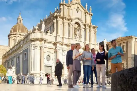 Eine Reisegruppe auf einem Platz in Catania auf Sizilien hört einer Reiseleiterin zu.