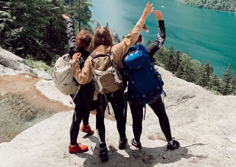 Gruppe von Wanderinnen mit Rucksäcken, die die Aussicht auf einen Wald und See genießen.