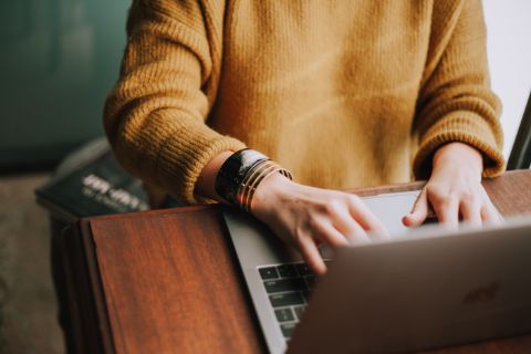 Eine Person in einem gelben Pullover, die am Laptop arbeitet.