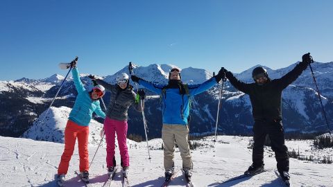 Gruppe von Skifahrern auf einem Berg mit schneebedeckten Alpen im Hintergrund.
