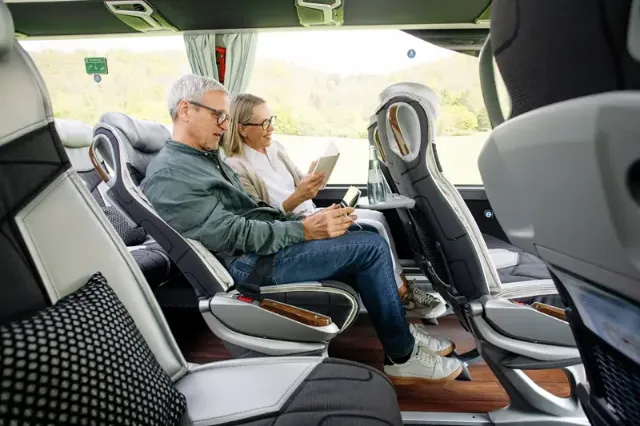 Ein Paar, das Bücher und Handys nutzt, sitzt auf bequemen Sitzen in einem Reisebus.