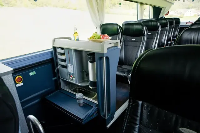 Innenansicht eines komfortablen Reisebusses mit Sitzen und einem Getränkehalter und Kaffeemaschine.