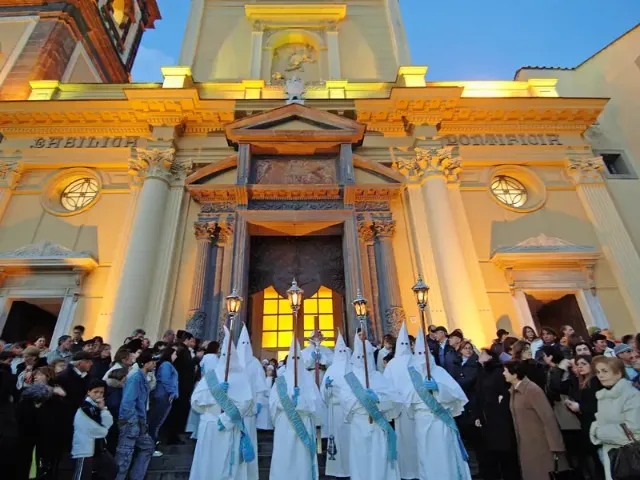 Für die traditionelle "Weiße Prozession" gekleidete Personen stehen mit Kreuzen vor einer Kirche.