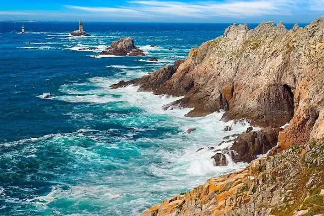 Eine raue Felsenküste mit Leuchtturm und blauem Meer am Pointe du Raz in der französischen Region Bretagne.