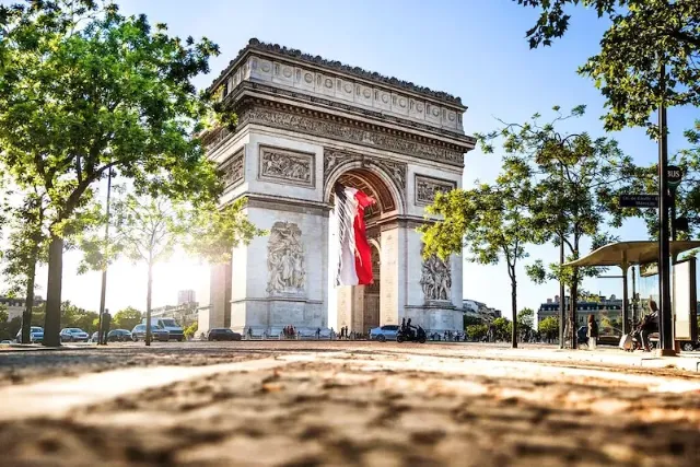 De Arc de Triomphe in Paris zwischen Bäumen und bei abendlicher Sonne.