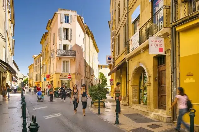 Eine sonnige Straße in der Innenstadt von AIx-en-Provence mit Fußgängern und Geschäften.