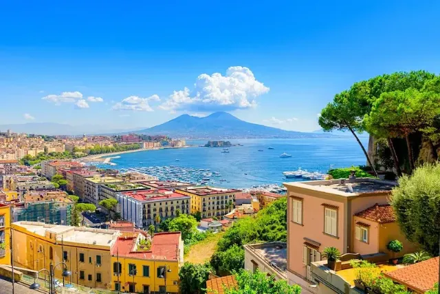 Blick auf den Golf von Neapel vom Hügel Posillipo aus, mit dem Vesuv im Hintergrund und farbigen Häusern im Vordergrund.