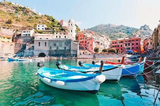 Der Ort Vernazza in der italienische Region Cinque Terre mir Ruderbooten im Vordergrund und Häuser und Bergen im Hintergrund.