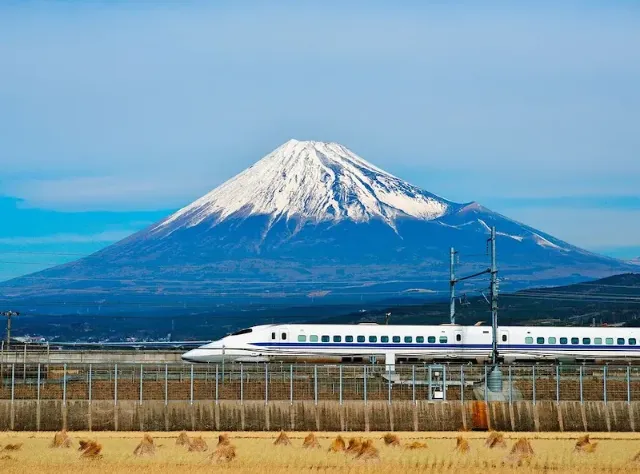 Ein japanischer Hochgeschwindigkeitszug fährt durch eine flache Landschaft am Fuji-Berg vorbei.