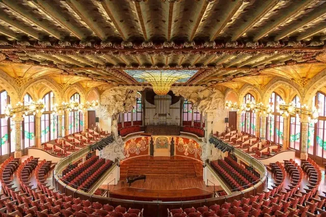 Der bestuhlte Konzertsaal vom Palau Musica Catalana in Barcelona mit farbenfrohen Glasfenstern und Deckenornamenten.