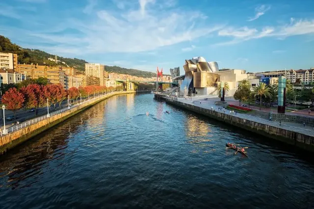 En Blick auf dem Guggenheim Museum in Bilbao am Fluss mit Ruderbooten und Gebäuden.