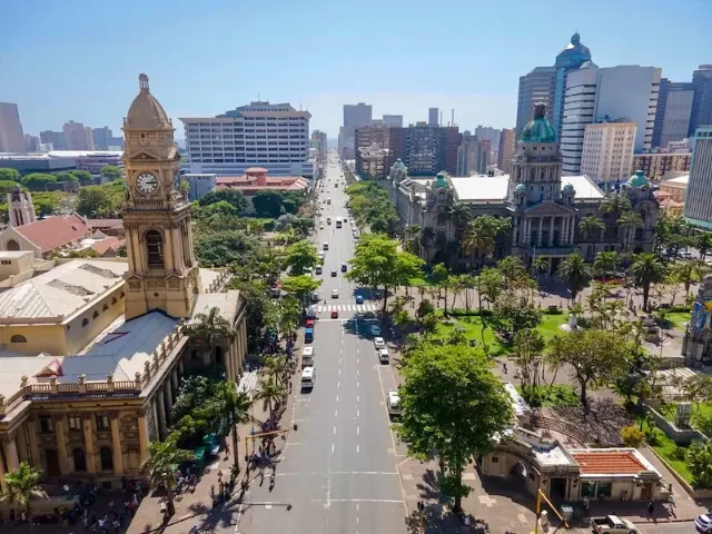 Eine breite Straße in der südafrikanischen Stadt Durban mit historischen und modernen Gebäuden und Hochhäusern bei sonnigem Wetter.