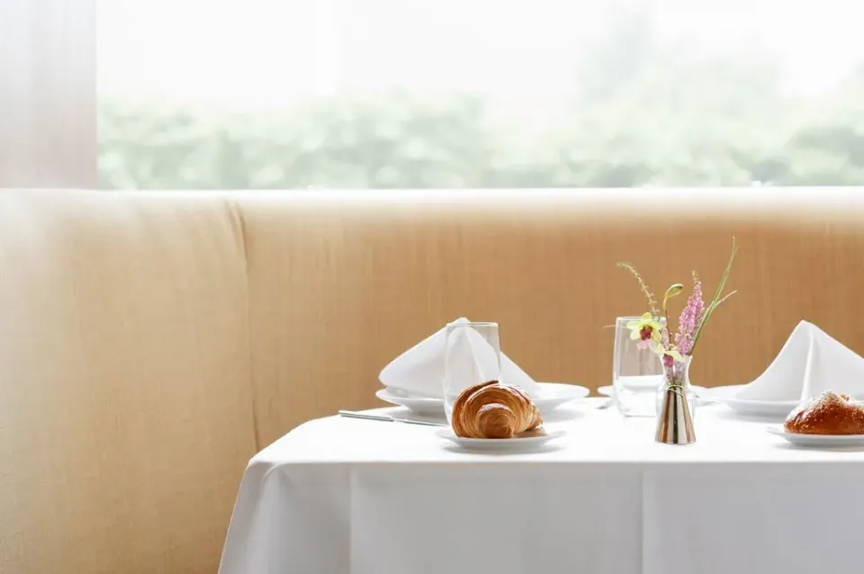 Ein gedeckter Frühstückstisch in einem Hotel mit weißer Stofftischdecke, Wassergläsern und frischem Gebäck.
