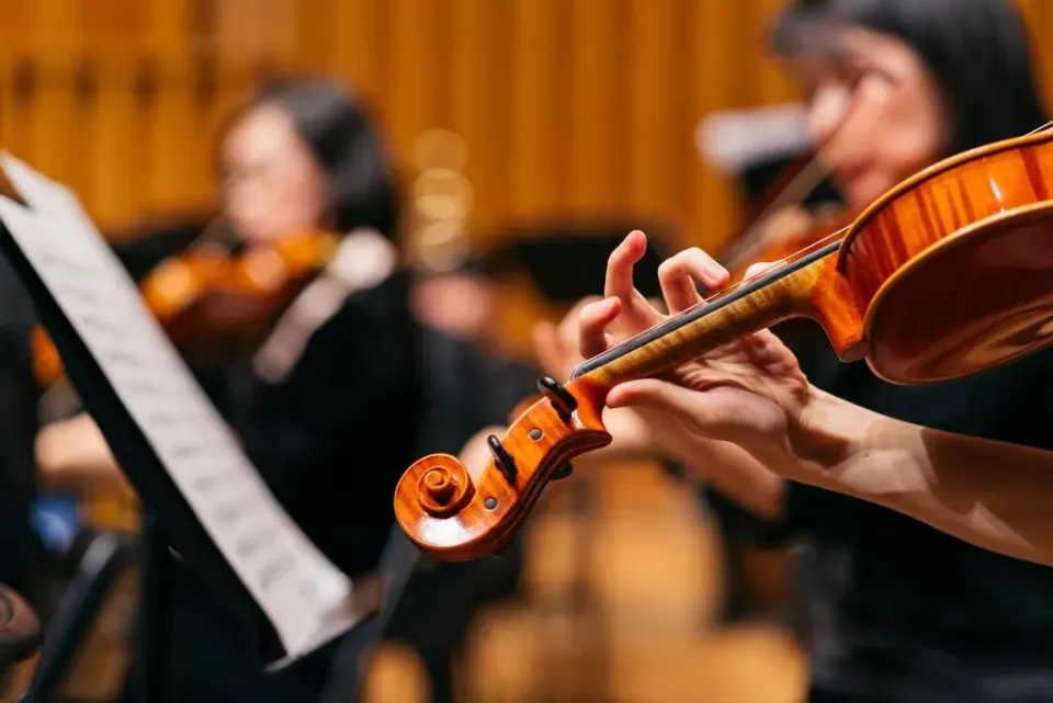 Eine Nahaufnahme einer Violine, die in einem Orchester von einer Musikerin bespielt wird.