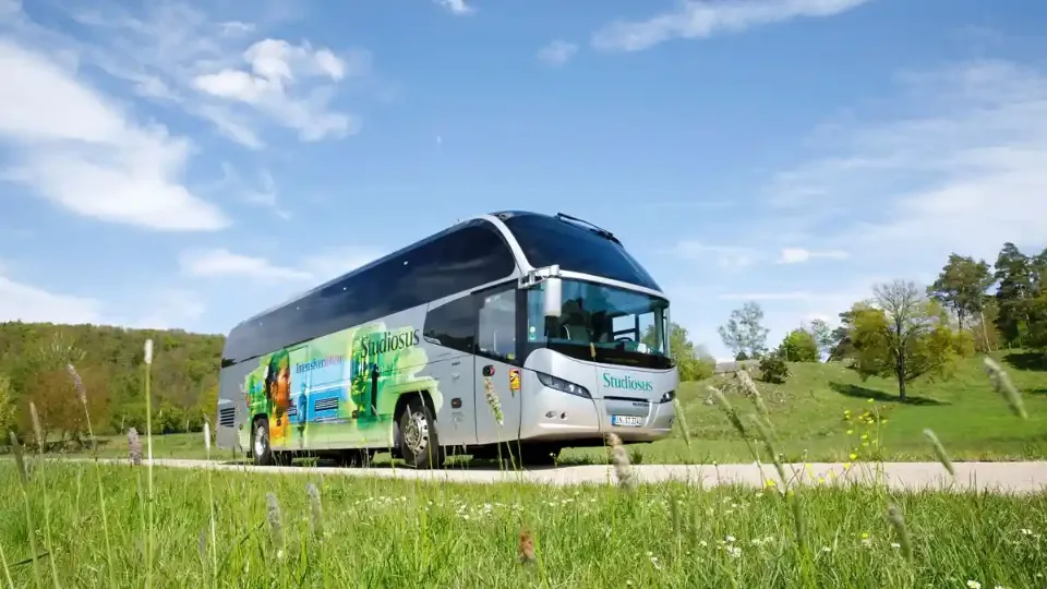 Ein moderner Reisebus von Studiosus fährt durch eine grüne Landschaft unter blauem Himmel.