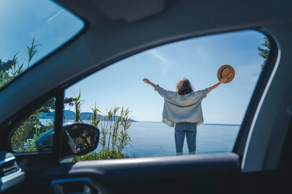 Eine Frau streckt sich am Ufer eines Sees, das Bild wurde aufgenommen aus einem Autofenster.