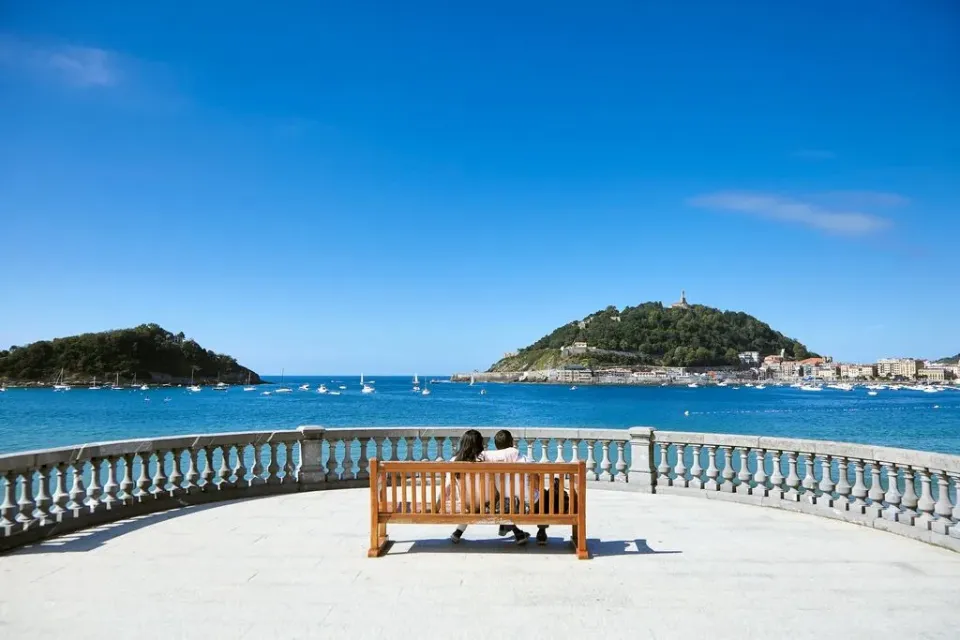 Ein Paar auf einer Bank genießt die Aussicht über das Meer und die sonnige Bucht von San Sebastian.