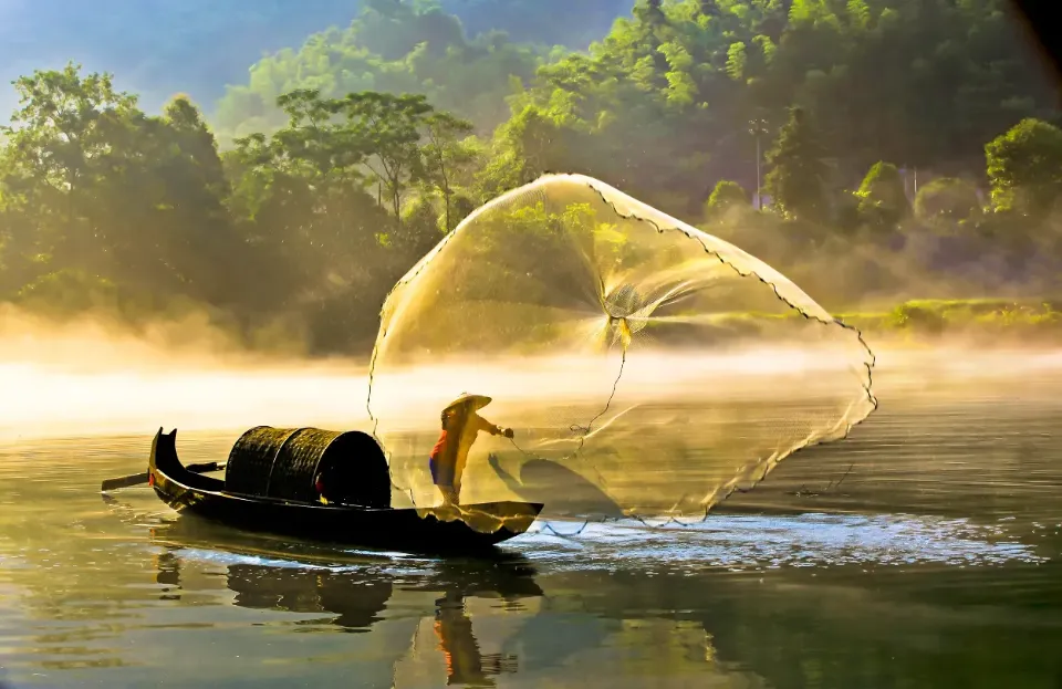 Ein asiatischer Fischer, der auf einem ruhigen Fluss sein Netz auswirft.