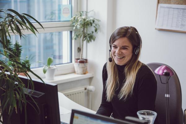 Frau mit Headset lächelt an ihrem Arbeitsplatz