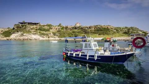 Unsere Reise führt uns auch in den Küstenort Paphos, wo die Cafés am Hafen zu einer Pause einladen und wir Fischerboote, die im glasklaren Wasser ankern, beobachten können.