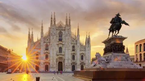 Die Piazza del Duomo bei Sonnenaufgang mit dem Mailänder Dom und dem monumentalen Reiterdenkmal für Vittorio Emanuele II., das auch "Il Cavallo di Bronzo" (Das Bronzepferd) genannt wird.