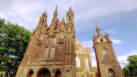 In Vilnius, der Hauptstadt von Litauen, besuchen wir das Gotische Ensemble, das aus der bekannten Annenkirche mit Glockenturm, der Kirche des heiligen Franziskus von Assisi und des heiligen Bernhard sowie dem Bernhardinerkloster besteht.
