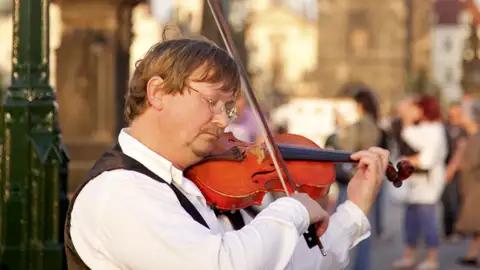 Ein Straßenmusiker spielt Geige auf der Karlsbrücke, ein typisches Erlebnis während der Stadterkundung in Prag.