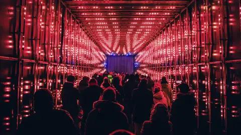 Eine Reisegruppe, von hinten gesehen, durchquert eine Lichtinstallation in einem Tunnel mit roten Lichtern. Ein Beispiel einers der Kunstwerke des Vilnius-Light-Festivals, dessen Besuch als Leistung dieser Reise inkludiert ist.