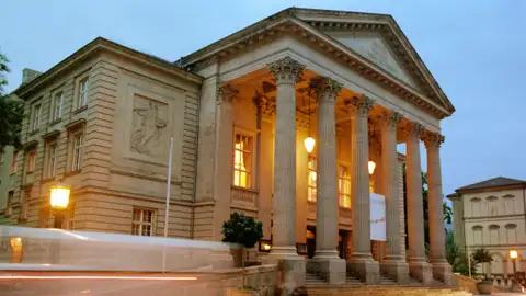 Auf unserer Gruppenreise mit Studiosus bewundern wir die Außenansicht eines neoklassizistischen Theaters in Meiningen mit Säulengang am Abend. Das prachtvolle Gebäude ist ein Highlight jeder Städtereise.